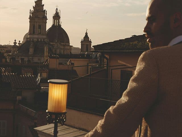 Man in a tweed jacket on a rooftop terrace at 369 Dine & Bar overlooking church domes and bell towers at sunset