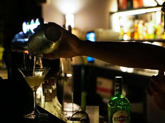 Atlas Rooftop Bar & Loungeでバーテンダーがシェーカーからマティーニグラスへカクテルを注ぎ、横にMartiniのボトル