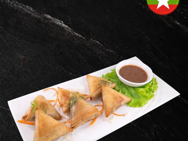 Crispy fried samosas with carrot garnish, lettuce and a dipping sauce on a white plate at Burbrit Myanmar