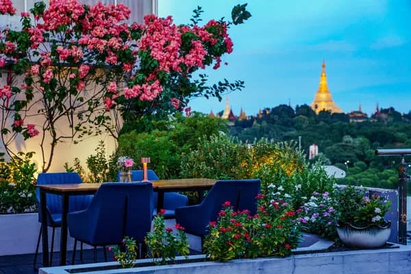 Rooftop terrace with blue chairs, flowers and a glowing golden pagoda on the horizon at Café Salween