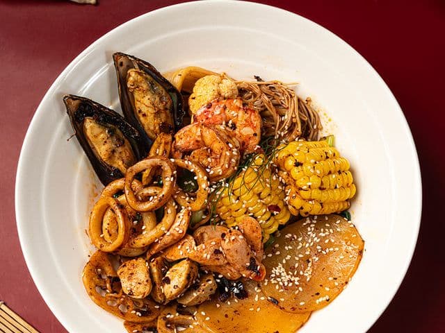 Seafood noodle bowl with mussels, squid rings, shrimp, corn and sesame-topped radish at Origin Coffee & Roastery