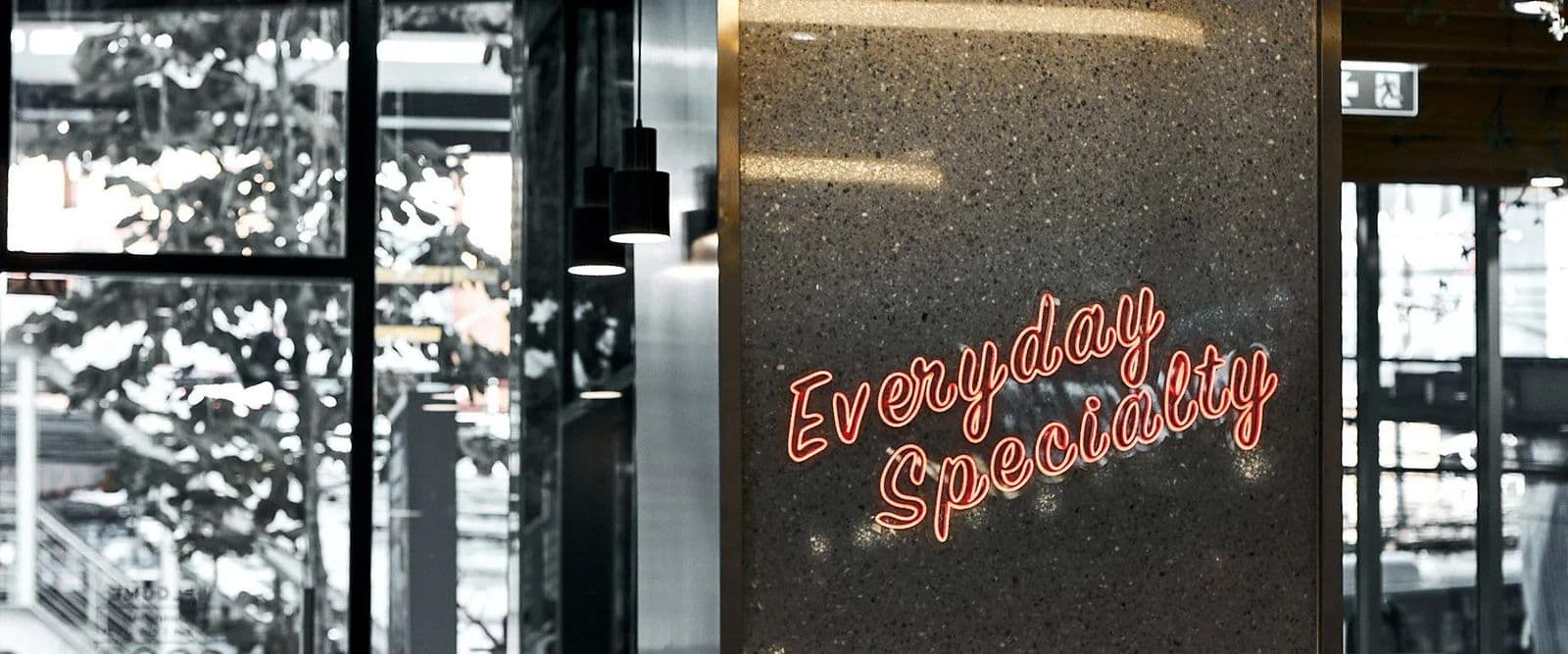Красная неоновая надпись «Everyday Special» на стене из терраццо и чёрные подвесные лампы в Pacamara Coffee Roasters