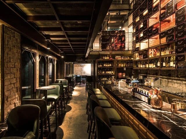Dim speakeasy bar at Rabbit Hole with green leather stools, a marble counter and towering backlit liquor shelves