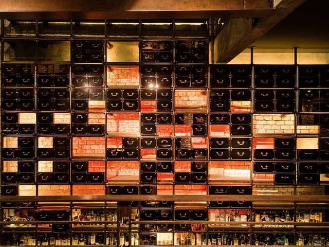 Wall of black drawers and exposed brick above rows of liquor bottles at Rabbit Hole bar