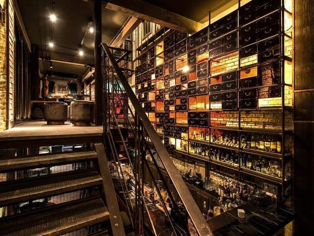 Metal staircase beside a towering wall of backlit drawers and liquor bottles at Rabbit Hole