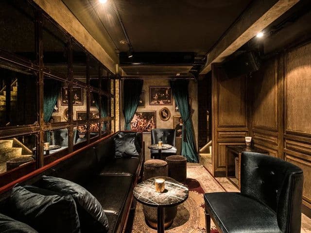 Dim lounge at Rabbit Hole with velvet banquette, marble side tables, teal curtains, framed paintings and a mirrored wall