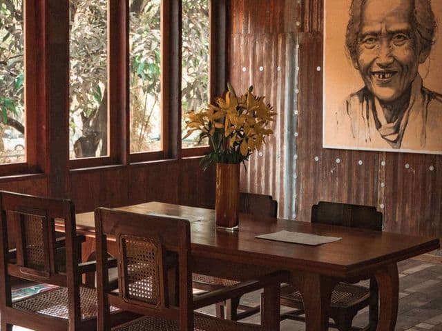 Wooden dining table with cane-back chairs, yellow lilies and a large charcoal portrait at Rangoon Tea House