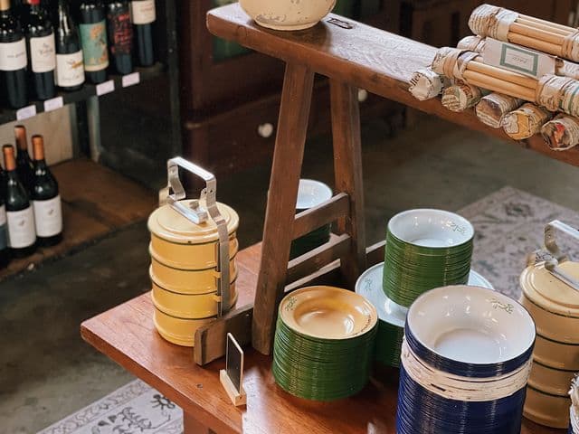 Stacked enamel plates, tiffin carriers and wine bottles displayed on wooden tables at Rangoon Tea House