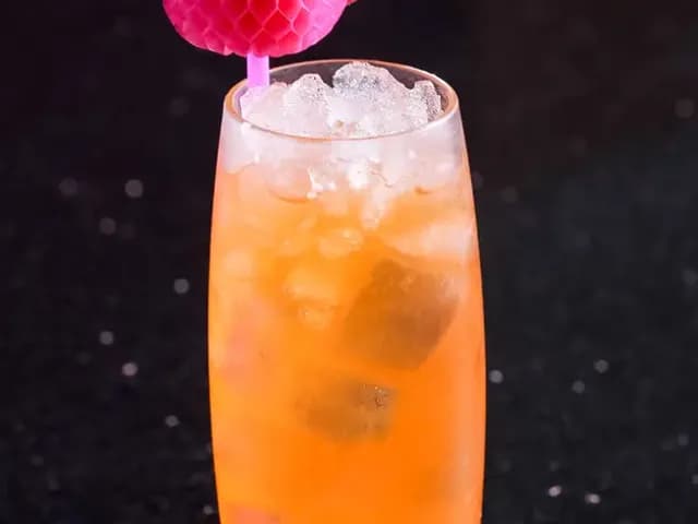 Orange cocktail over crushed ice in a tall glass with a pink honeycomb pick at Red Sky Bar