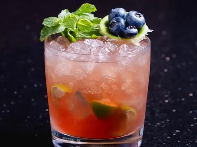 Pink cocktail with crushed ice and lime, garnished with mint and blueberries, at Red Sky Bar