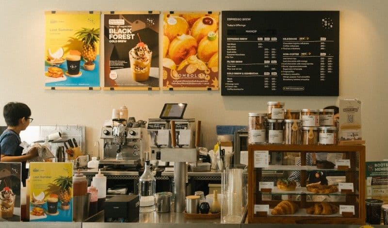 Rootsのカフェカウンター。エスプレッソマシン、クロワッサンが並ぶペストリーケース、上にはメニューボードとBlack Forestコールドブリューのポスター