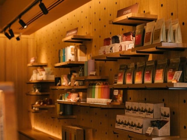 Roots の暖かな照明に照らされた木製ペグボード棚に、販売用のコーヒー豆の袋や箱入り商品が並ぶ