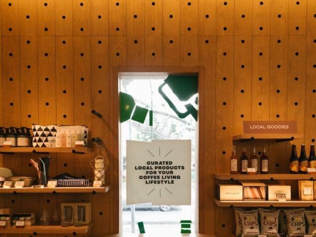 Rootsの木製パネルの物販コーナー、ガラス扉の横に地元の商品や瓶入りドリンク、チップスが並ぶ棚