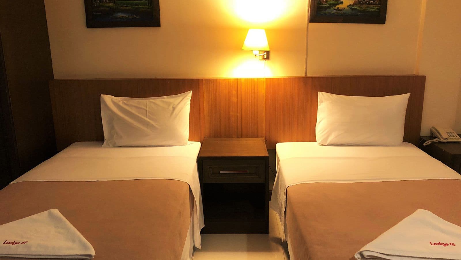 Lodge 61 Bed & Breakfast Hotelの客室、白い枕と茶色のベッドスローのツインベッドと木製ナイトテーブル、壁掛けランプ