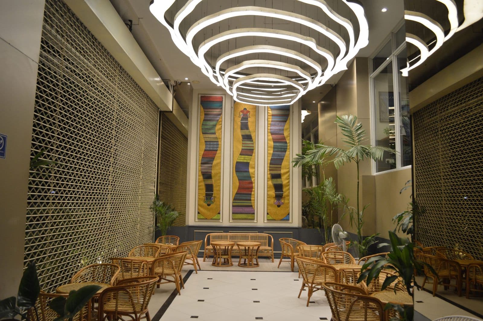 The Pier Rooftop Bar & Terrace 室内座位区,摆有藤椅、圆桌、盆栽棕榈和波浪环形吊灯
